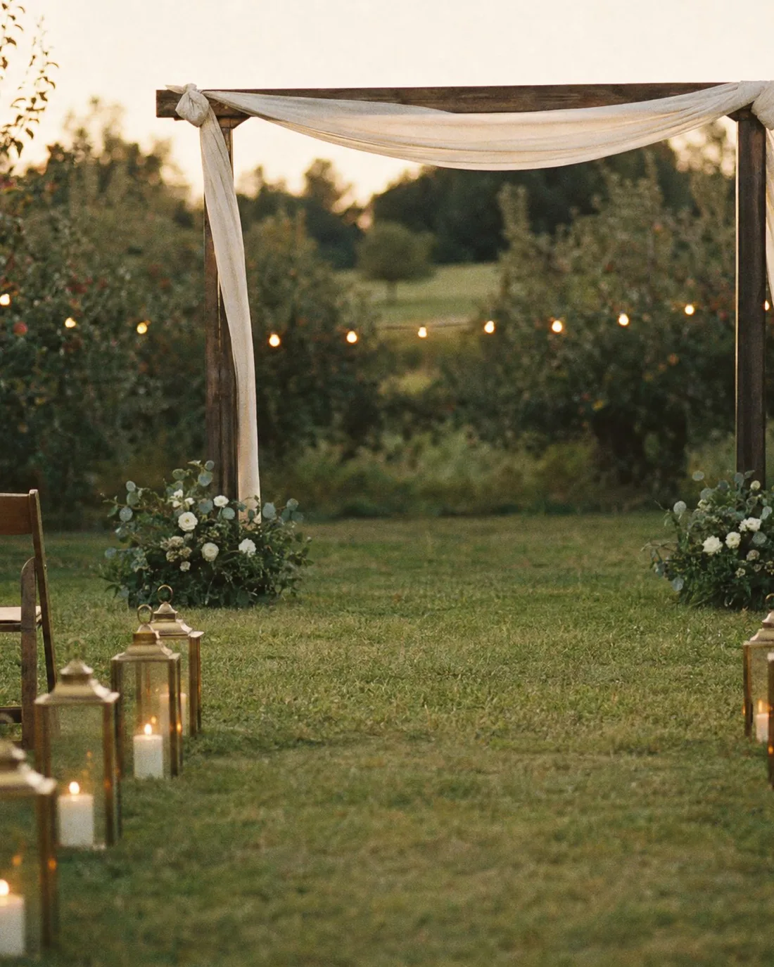 A wedding arch built from orchard saplings and chiffon, standing in the long grass at Blackbird Hollow